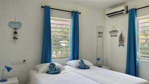 A bedroom with two beds, a ceiling fan, an air conditioning unit, and a window with blue curtains.