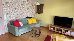A living room with a sofa, a small round table, a TV, and a bookshelf.