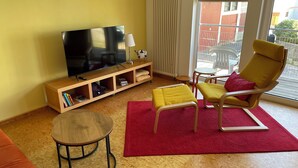 A living room with a flat-screen TV, wooden entertainment unit, yellow armchair, red rug, and a small wooden table. - The Blue House - from hay barn to vacation apartment - now with SAUNA (Pirmasens)