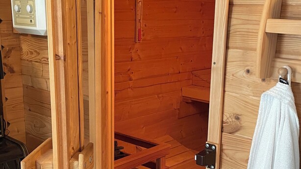 A wooden sauna room with a bench, a towel rack, and a thermostat on the wall. - The Blue House - from hay barn to vacation apartment - now with SAUNA (Pirmasens)