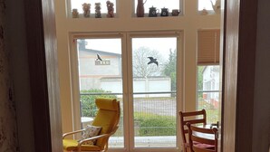 A room with a wooden floor, a yellow chair, a wooden table, and a view through a glass door to an outdoor area with a yellow chair and a table. - The Blue House - from hay barn to vacation apartment - now with SAUNA (Pirmasens)