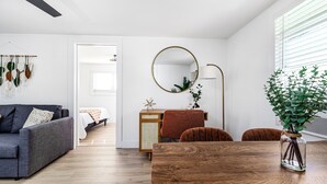 Ein modernes Wohnzimmer mit einem Holzespeisetisch, einem grauen Sofa, einer kleinen Kommode und einem Spiegel.