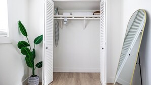 Ein weißer Kleiderschrank mit geöffneten Türen, ein Blumentopf und ein Surfbrett, das an der Wand lehnt.