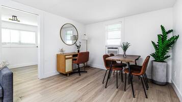 Une pièce moderne et bien éclairée, comprenant une table à manger, des chaises, un buffet et une grande plante en pot.
