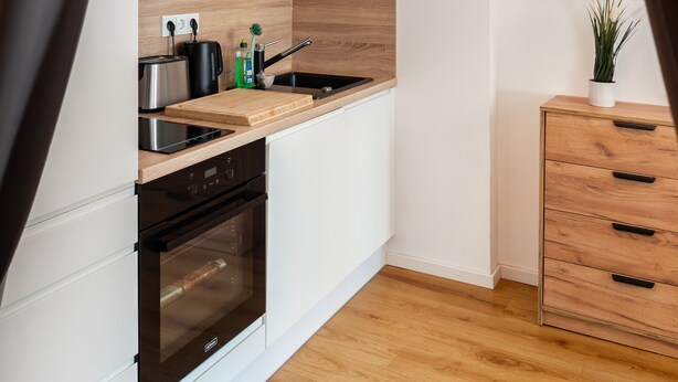 Une cuisine moderne avec des armoires blanches, un plan de travail en bois, un four encastré et un luminaire suspendu.