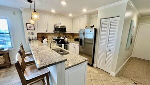 A kitchen with white cabinets, a granite countertop, stainless steel appliances, and a dining area with wooden chairs. - FREE DAILY FUN with this beach lovers dream getaway! (Saint Augustine)