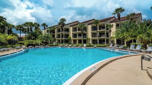 A large outdoor swimming pool surrounded by lounge chairs and palm trees, with a multi-story building in the background. - FREE DAILY FUN with this beach lovers dream getaway! (Saint Augustine)