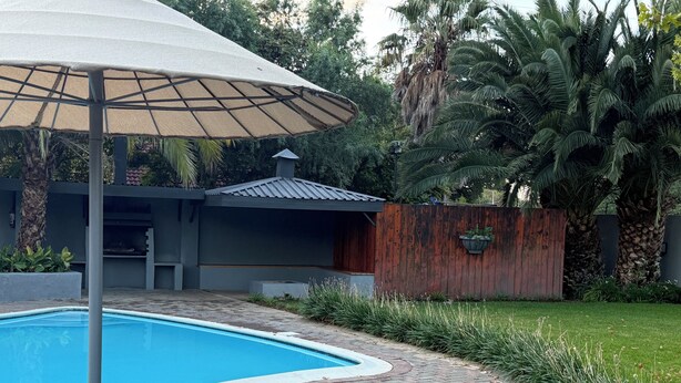 A swimming pool with lounge chairs and an umbrella. - Charming B&B with WiFi and AC in Welkom, South Africa (Welkom)