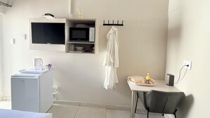 A compact hotel room with a kitchenette, a small table with a chair, a microwave, a kettle, and a bottle of hand sanitizer. - Charming B&B with WiFi and AC in Welkom, South Africa (Welkom)