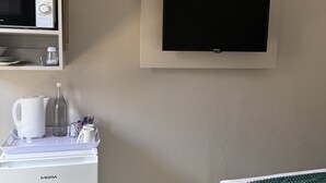 A bedroom with a bed, a TV mounted on the wall, a small refrigerator, and a shelf with a kettle and other items. - Charming B&B with WiFi and AC in Welkom, South Africa (Welkom)