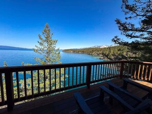 Une terrasse en bois avec une balustrade donnant sur un lac, entourée d’arbres et de montagnes.