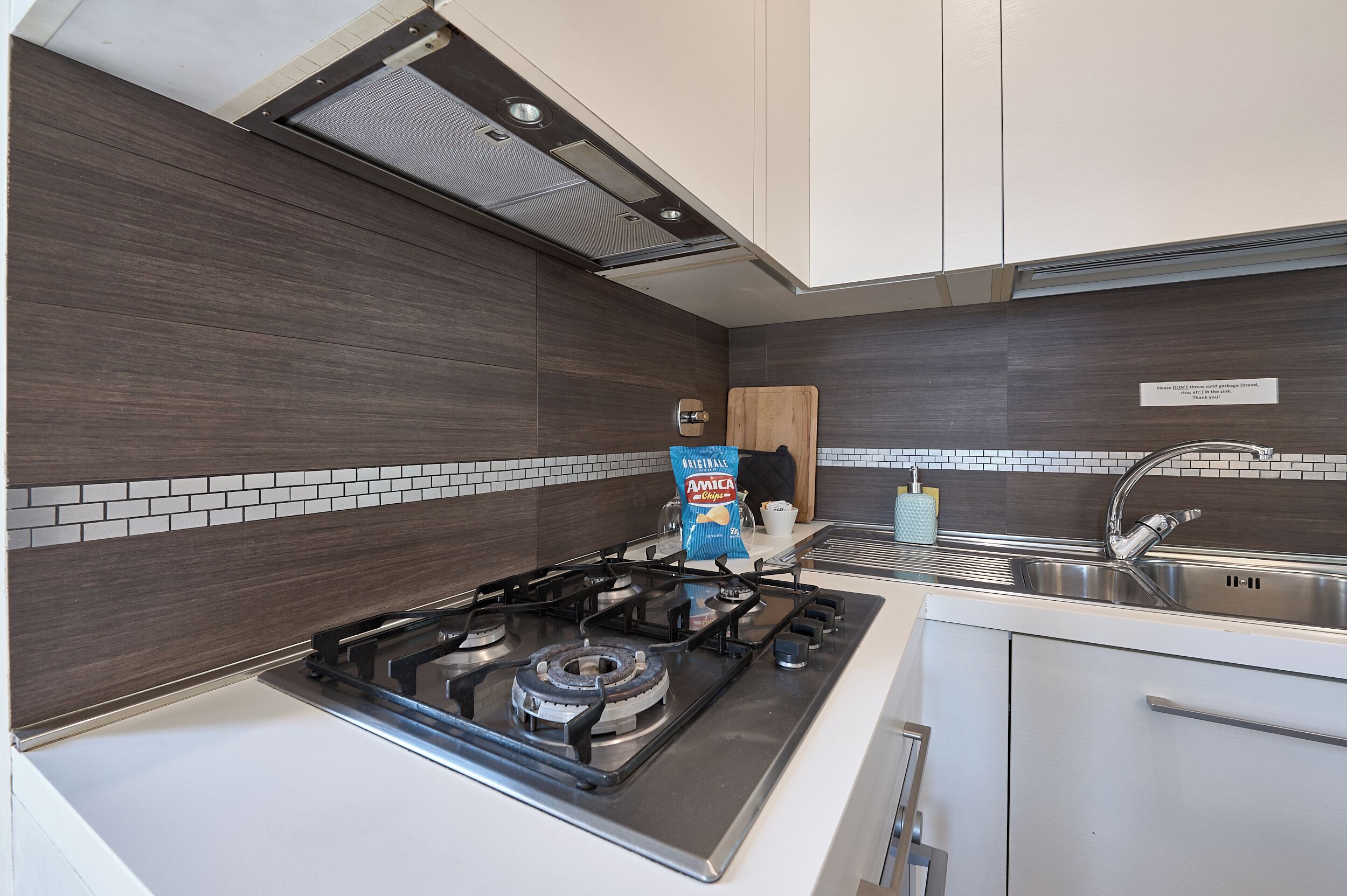 A modern kitchen with a gas stove, a sink, and a wooden cutting board.
