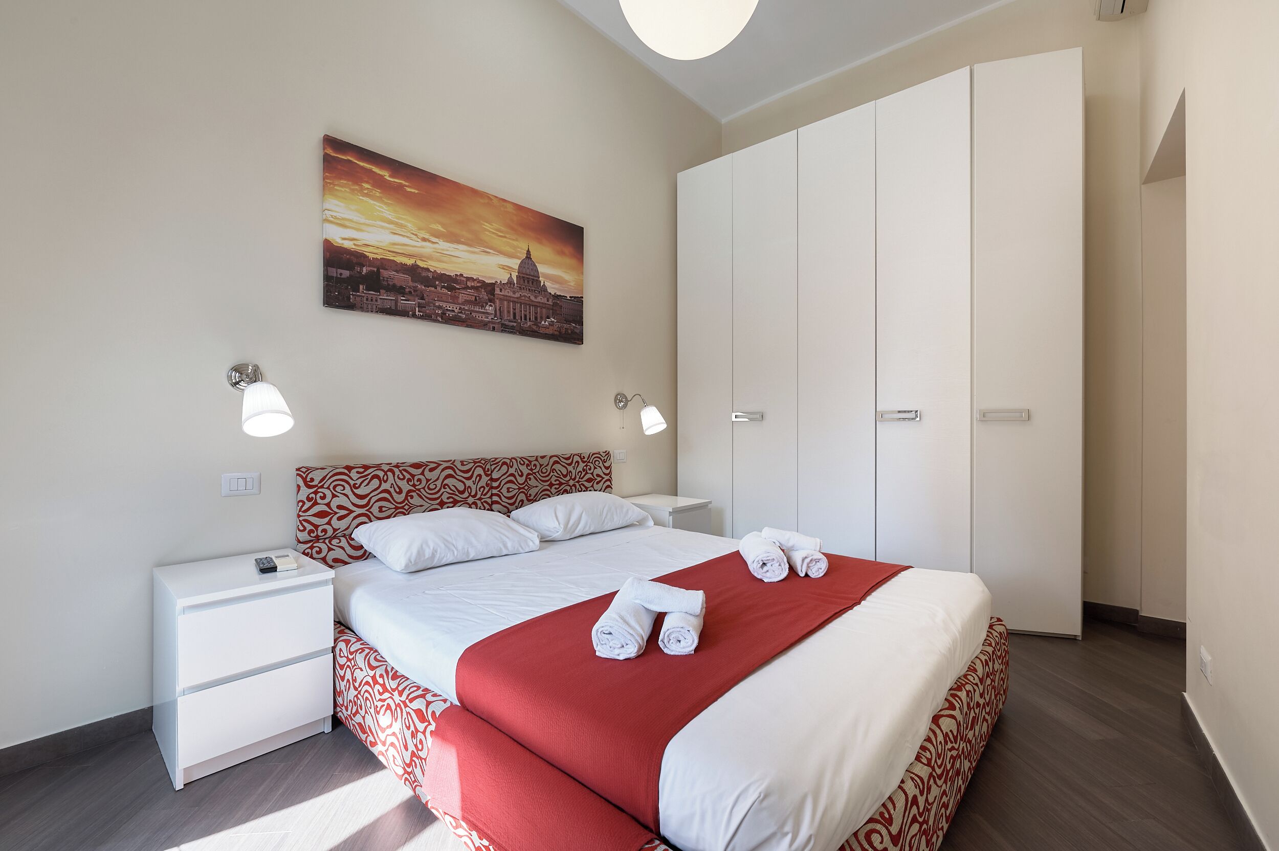 Een hotelkamer met een bed, nachtkastje, kledingkast en een stadsgezicht op het doek.