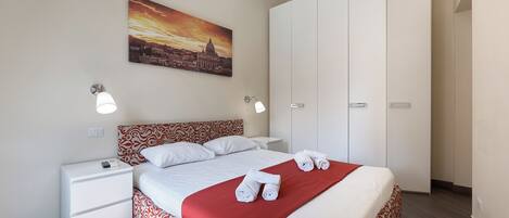 Een hotelkamer met een bed, nachtkastje, kledingkast en een stadsgezicht op het doek.