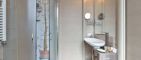 A modern bathroom with a glass shower enclosure, a white sink, and a mirror with lights.