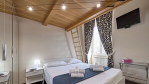 A modern hotel room with a wooden ceiling, a bed with white linens, a bedside table with a lamp, a glass desk with a pink box, and a TV mounted on the wall. - A casa Di Roberta  (Rome)