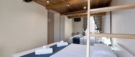 A hotel room with a wooden ceiling, a bed with white linens, a bedside table with a lamp, and a mirror reflecting the room.