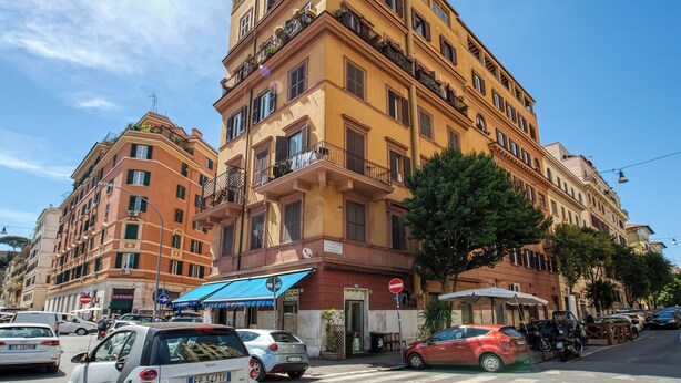 A multi-story building with balconies, a blue awning, and a street view with parked cars. - A casa Di Roberta  (Rome)