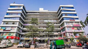 Un edificio de varios pisos con diversos comercios en la planta baja, incluyendo una farmacia y una tienda familiar.