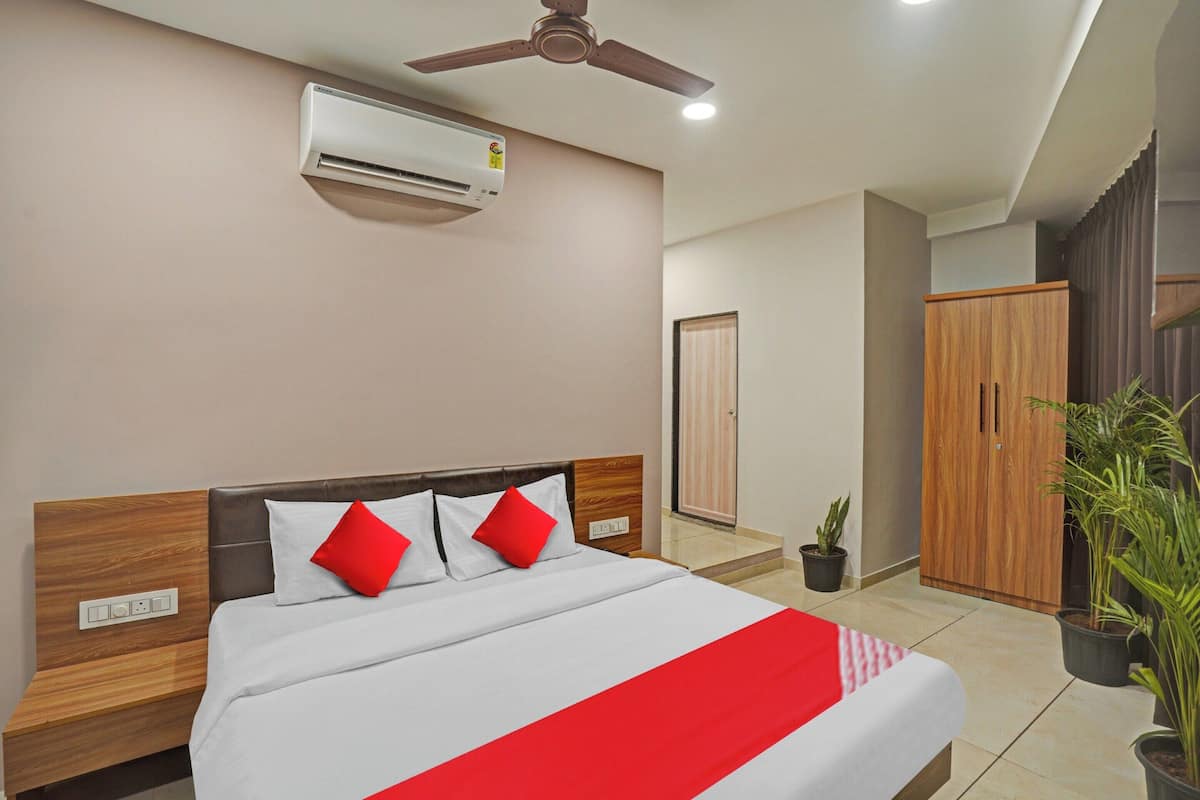 Habitación de hotel con cama, ventilador de techo, aire acondicionado, armario y plantas en macetas.
