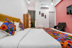 Hotellihuone, jossa on sänky, tuoli, televisio ja ikkuna, jossa on verhot.