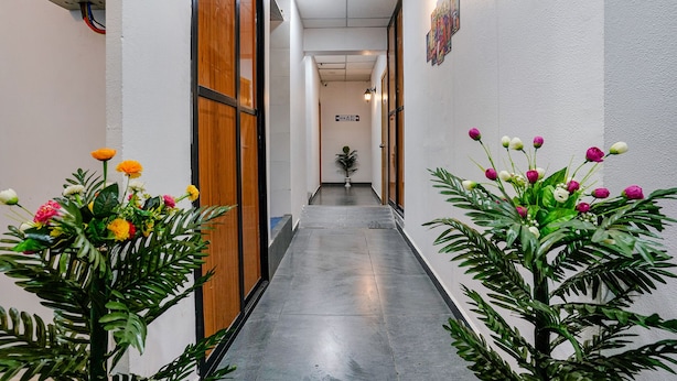 Un pasillo estrecho con puertas y paredes de madera que conduce a una habitación. Hay plantas en macetas con flores a ambos lados.