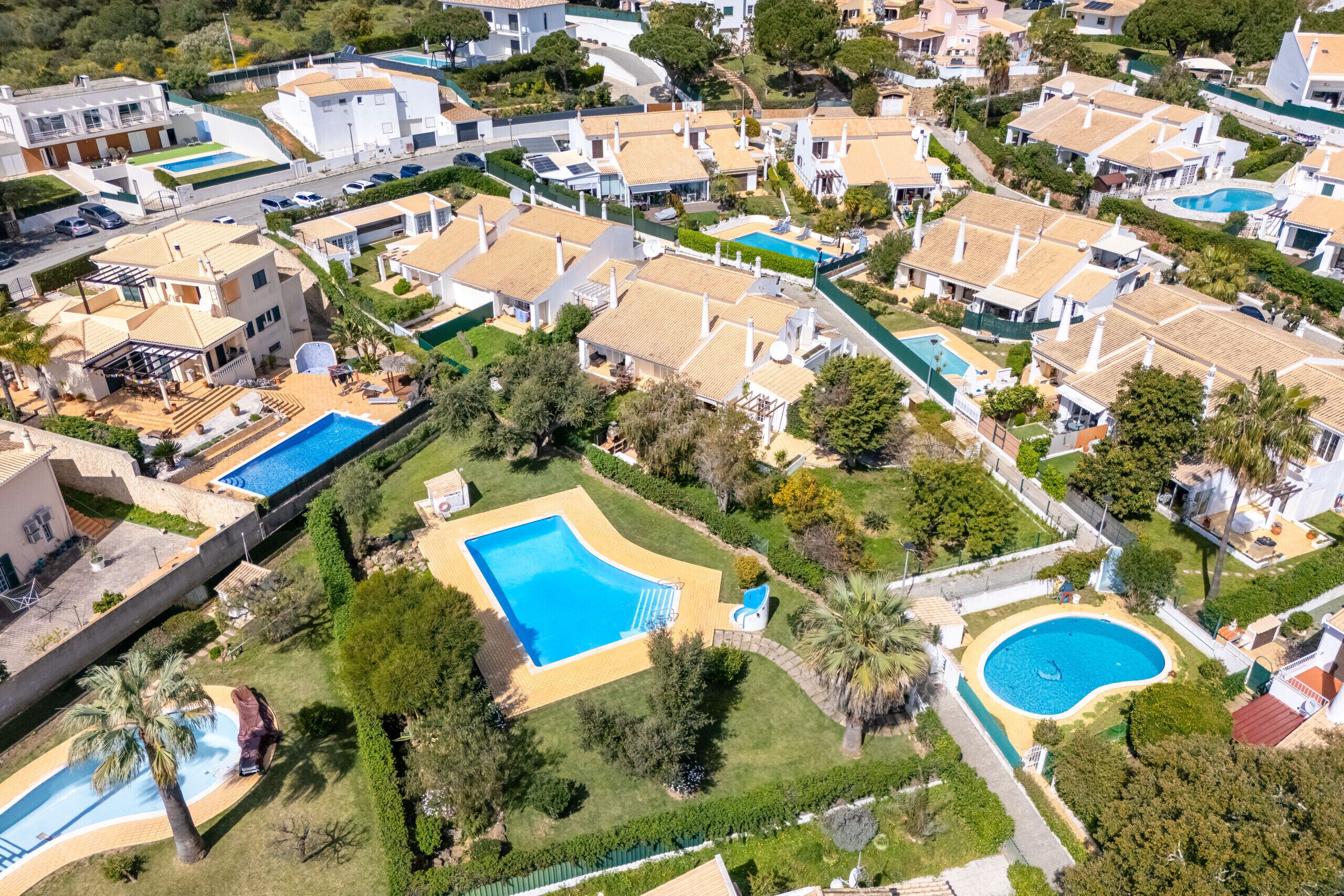 Vista aérea de um bairro residencial com várias casas, piscinas e jardins bem cuidados.