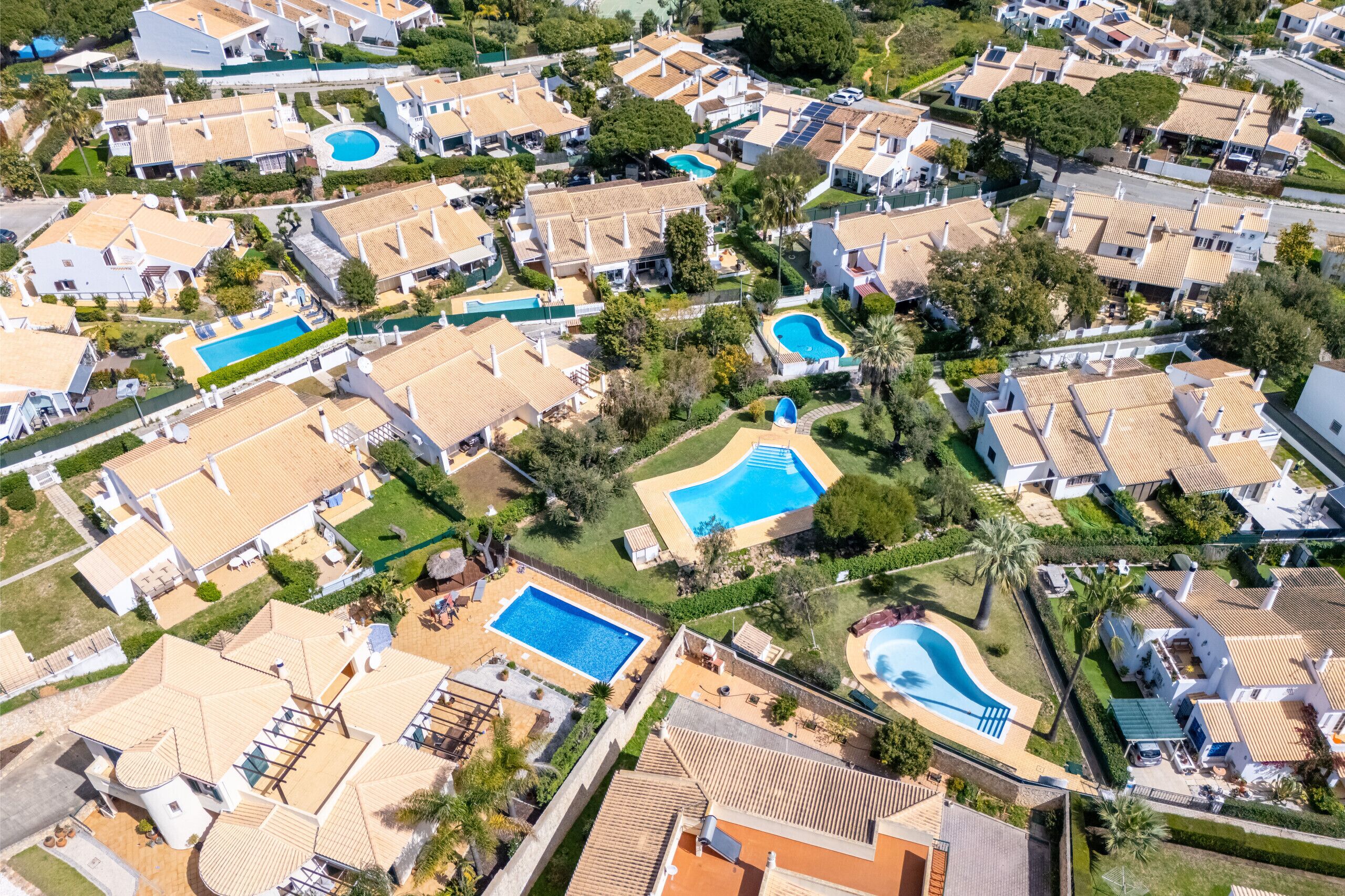 An aerial view of a residential area with multiple houses, swimming pools, and lush greenery.