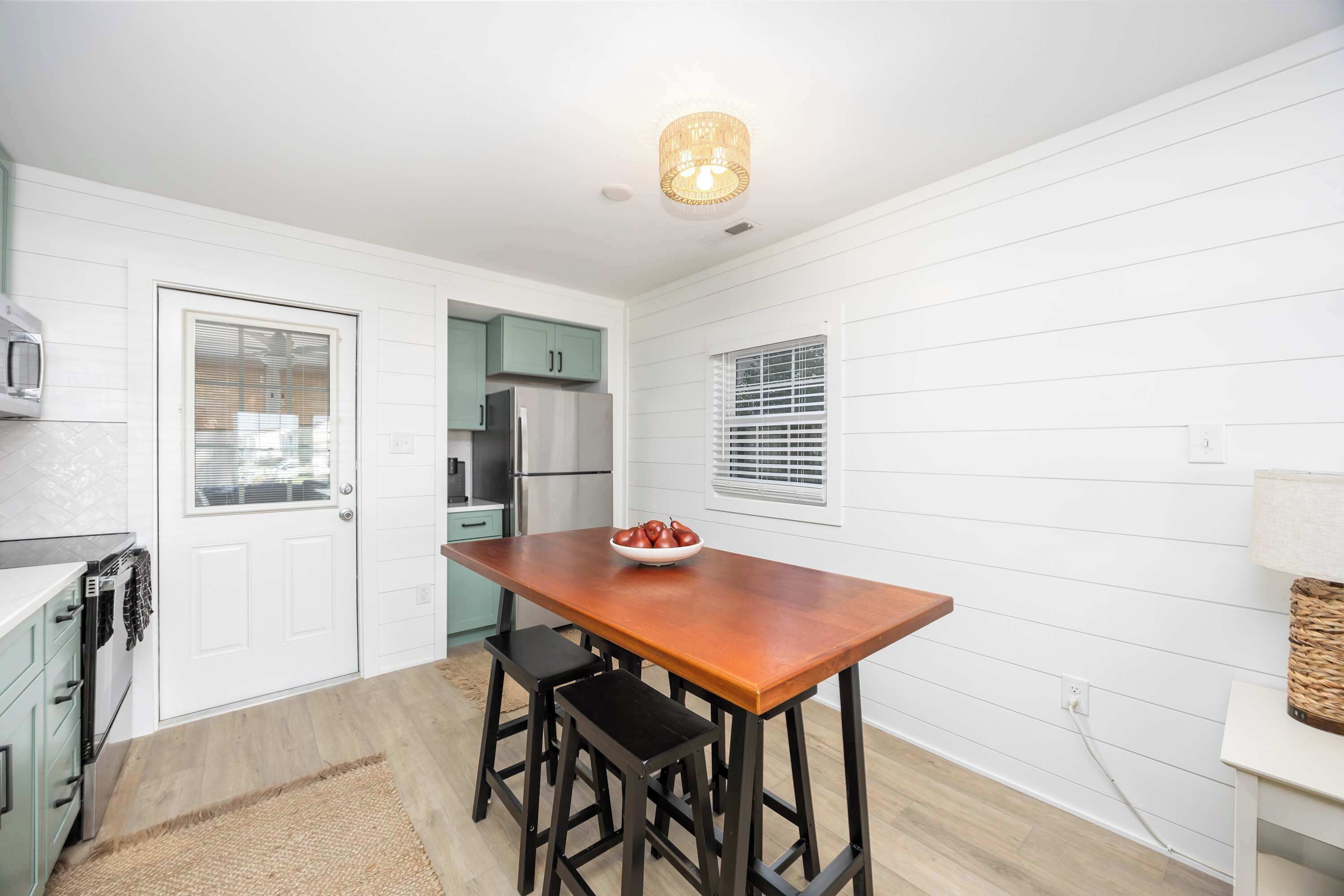 A kitchen with a wooden table, two bar stools, a bowl of fruit, and a hanging light fixture.