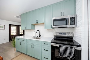 Une cuisine avec des armoires de couleur turquoise, un four à micro-ondes en acier inoxydable et un four traditionnel.