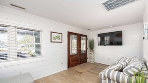 Une pièce avec un plancher en bois, un canapé, un banc, un téléviseur et une porte à panneaux de verre.