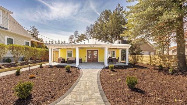 Une maison à deux étages avec une façade jaune, un porche et une allée pavée.