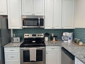 A kitchen with white cabinets, a stainless steel stove, a microwave, a toaster, and a coffee maker.