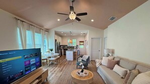 A spacious living room with a flat-screen TV, a ceiling fan, a dining area, and a kitchen in the background. - The Orange Blossom Suite | Near UF, Shands, D-town (Gainesville)