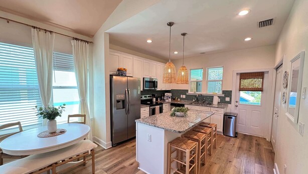 A modern kitchen with a central island, stainless steel appliances, and a dining area with a round table and chairs. - The Orange Blossom Suite | Near UF, Shands, D-town (Gainesville)