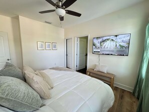 Un dormitorio con cama, almohadas, ventilador de techo, televisor en la pared y puerta que da a otra habitación.