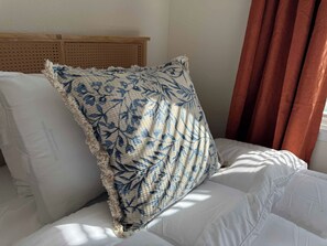 Un lit avec une literie blanche et un oreiller à motifs bleus et beiges.