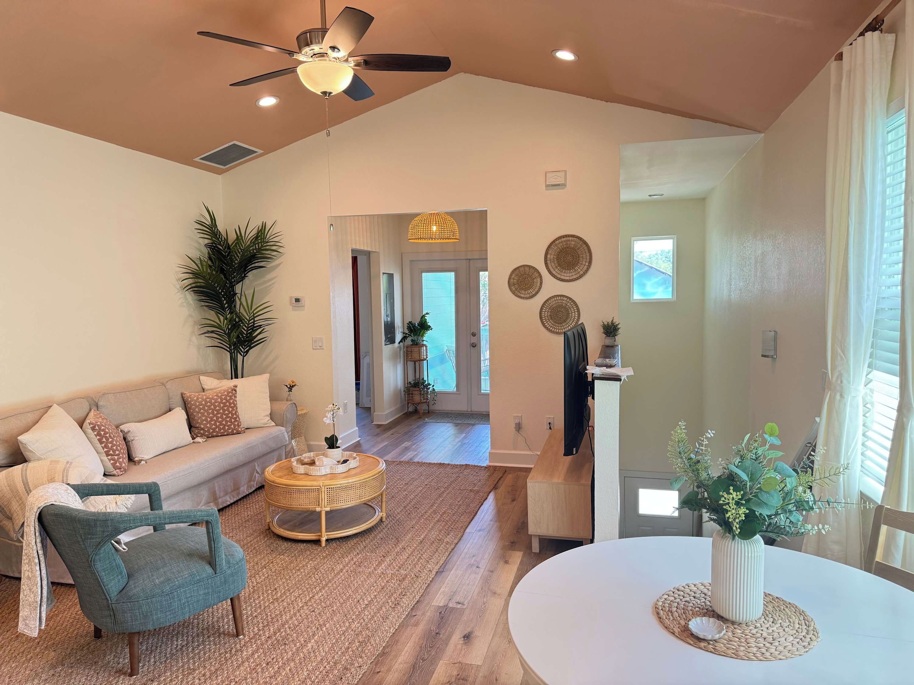 A spacious living room with a high ceiling, a ceiling fan, and a large window with curtains.