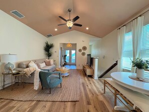 A spacious living room with a high ceiling, a ceiling fan, a sofa, a coffee table, a TV stand, and a dining area.