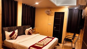 Una habitación de hotel con una cama grande, cortinas oscuras, un ventilador de techo, una mesita de noche de madera, un televisor y un armario empotrado.