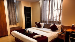 Una habitación de hotel con una cama grande, una mesita de noche con un teléfono, una mesita auxiliar de madera, un armario y una ventana con cortinas.