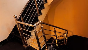 Una escalera con barandillas metálicas y peldaños negros, que conduce a un rellano con una pared blanca y otra amarilla.