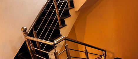 A staircase with metal railings and black steps, leading to a landing with a white wall and a yellow wall.