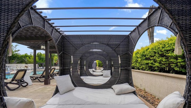 Un espacio de descanso circular al aire libre con una cama y cojines, rodeado por una estructura de pérgola.