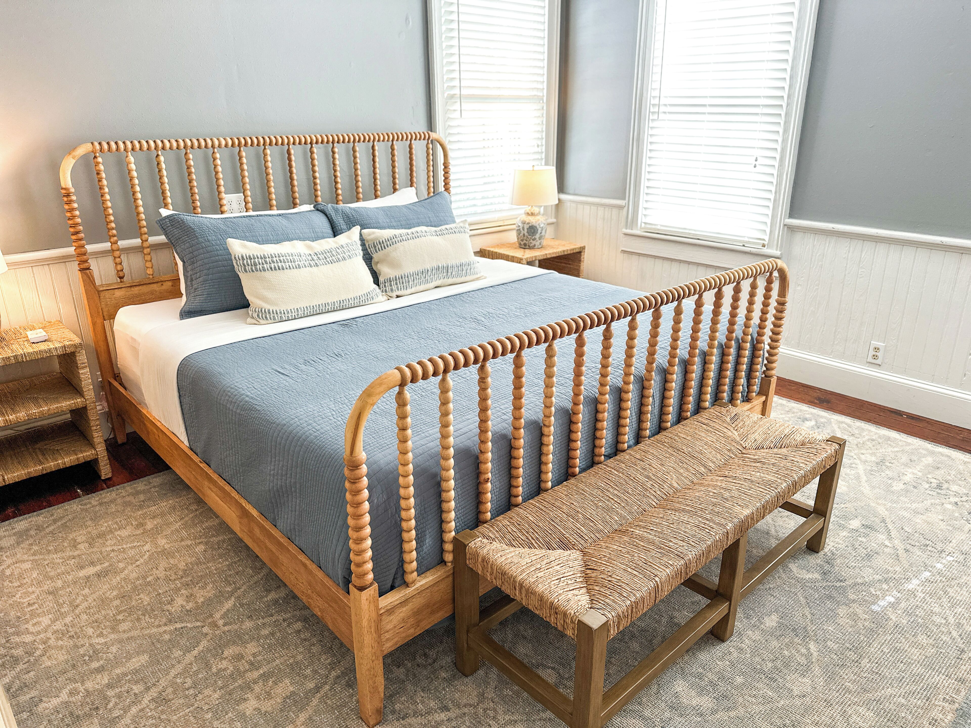 A bedroom with a wooden bed frame, a blue bedspread, and a woven bench.