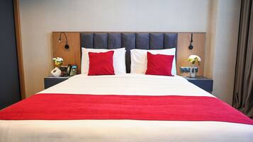 A hotel room with a large bed, red and white bedding, two nightstands with lamps, and a vase with flowers on each side.