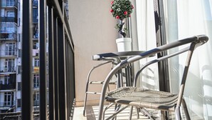 A balcony with a metal chair and a small table, a potted plant with red flowers, and a view of a residential building. - Landmark Hotel (Batumi)