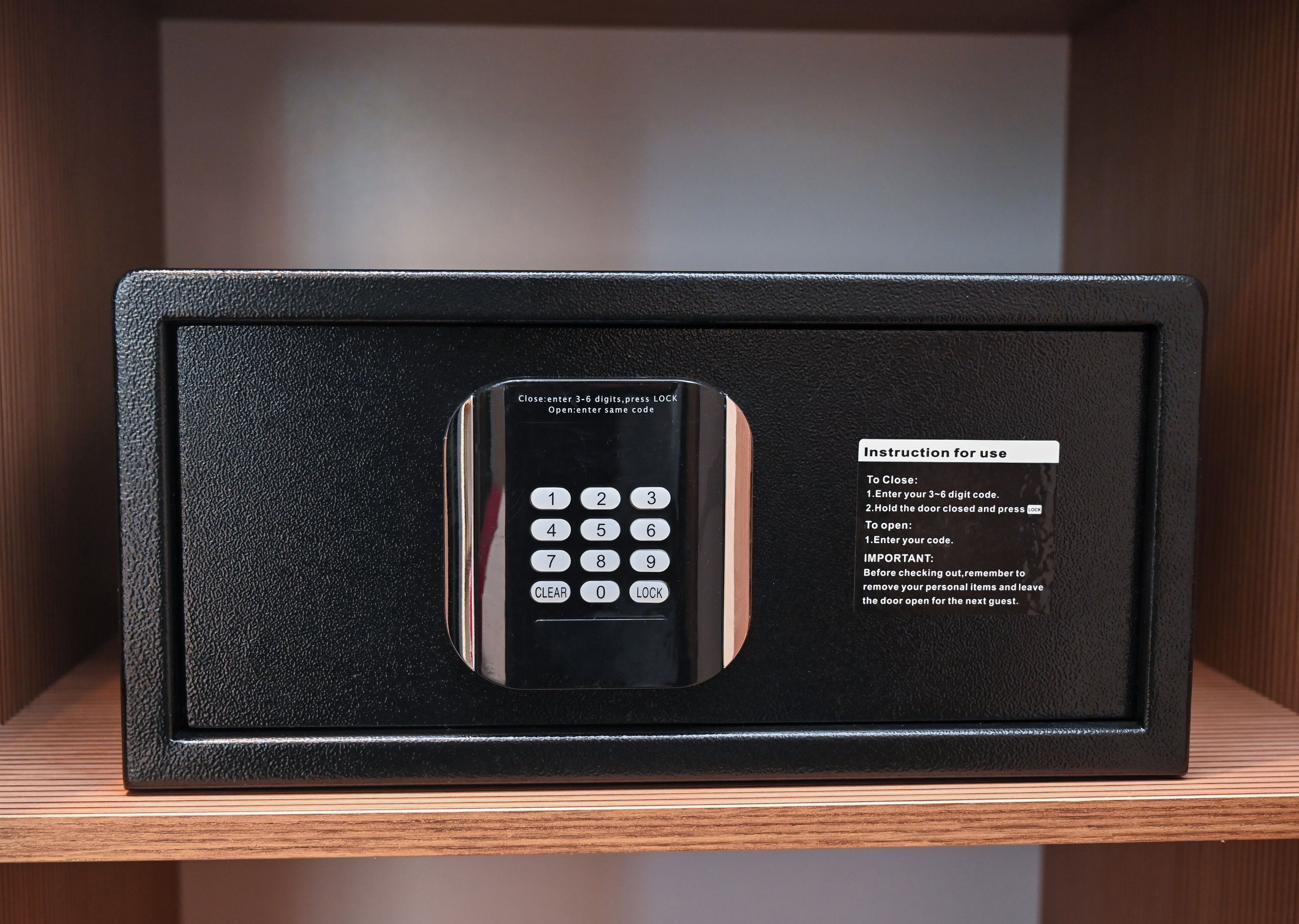A black electronic keypad with instructions for use, placed in a black box on a wooden shelf.