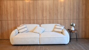 A light-colored sectional sofa with striped pillows against a wooden wall with circular light fixtures. - Landmark Hotel (Batumi)