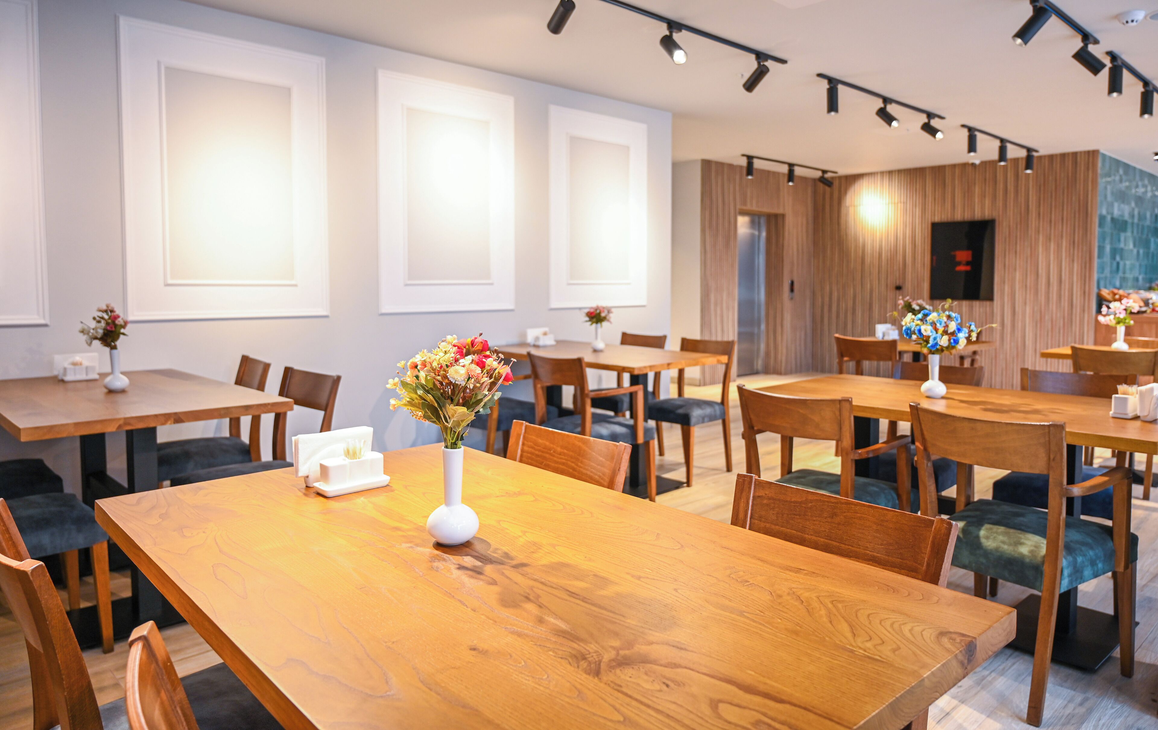 A modern dining area with wooden tables and chairs, white walls, and large windows.